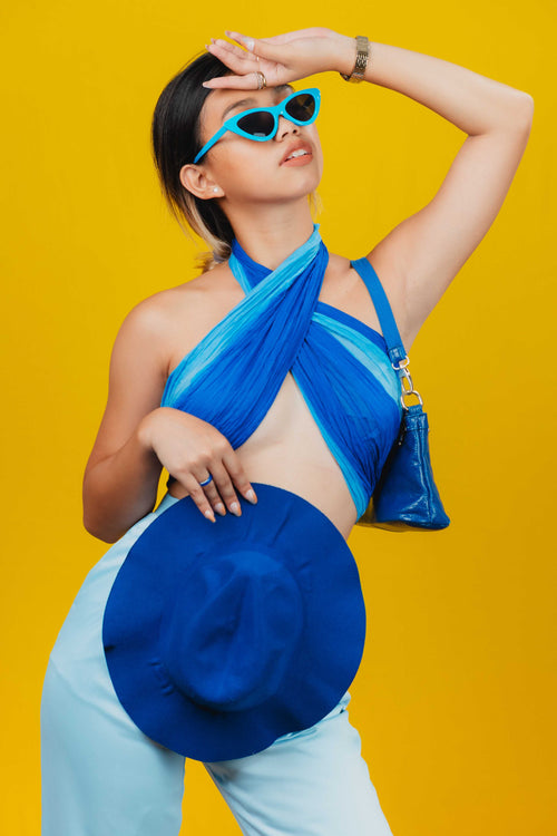 Stylish woman in blue attire holding hat and sunglasses, gazing at the sky 